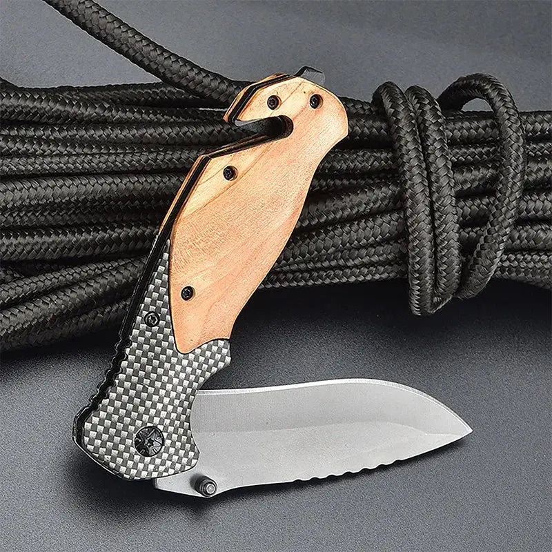 Folding knife with a partially serrated stainless steel blade, wooden and carbon fiber-patterned handle, placed against a bundle of black braided rope.