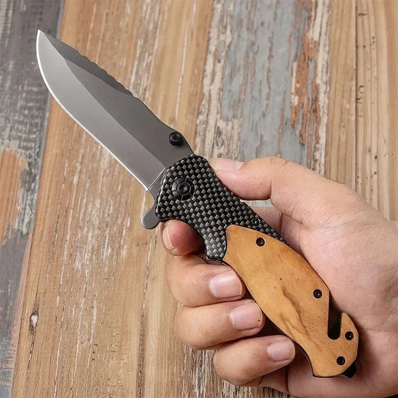 Folding knife with a partially serrated stainless steel blade, wooden and carbon fiber-patterned handle, placed against a bundle of black braided rope.